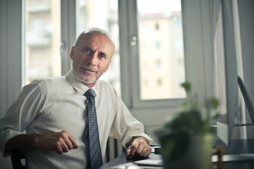 Hombre sentado en una mesa de trabajo, con corbata y mirando con gesto de duda.  Foto seleccionada para representar la página Contrato de confidencialidad